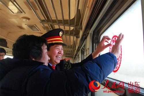 腊月二十三，从山东泰山开往淄博的7054次绿皮车上，列车长赵新华和乘客们一起贴窗花迎传统“小年”。（摄影：宋翠）